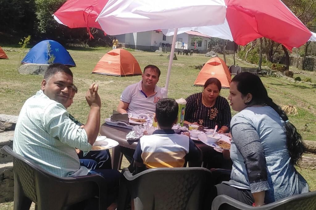 A group of people seated at an outdoor table with a tent and umbrellas in the background.