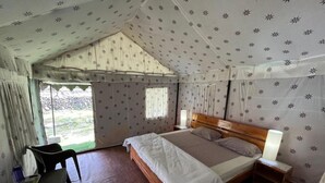 Una habitación tipo tienda de campaña con una cama, mesita de noche, lámpara y una silla.
