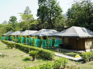 A row of tents with a paved walkway in between, surrounded by greenery and trees.