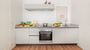 Una cocina moderna con armarios blancos, horno empotrado, campana de acero inoxidable y un pequeño ventanal sobre el lavadero.