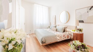 Un dormitorio con cama, mesita de noche, espejo y ventana con cortinas.