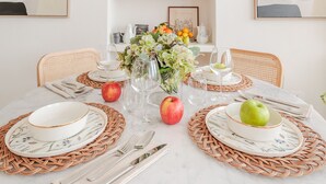 Una mesa redonda para comer con individuales, platos, cubiertos y un florero con flores.