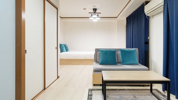 A compact room with a bed, a sofa, a small table, a ceiling fan, and a window with curtains. - Urban Plaza (Osaka)
