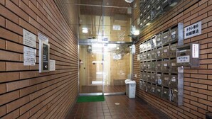 A hallway with a tiled floor, a trash bin, and a row of metal lockers on the right. - Urban Plaza (Osaka)
