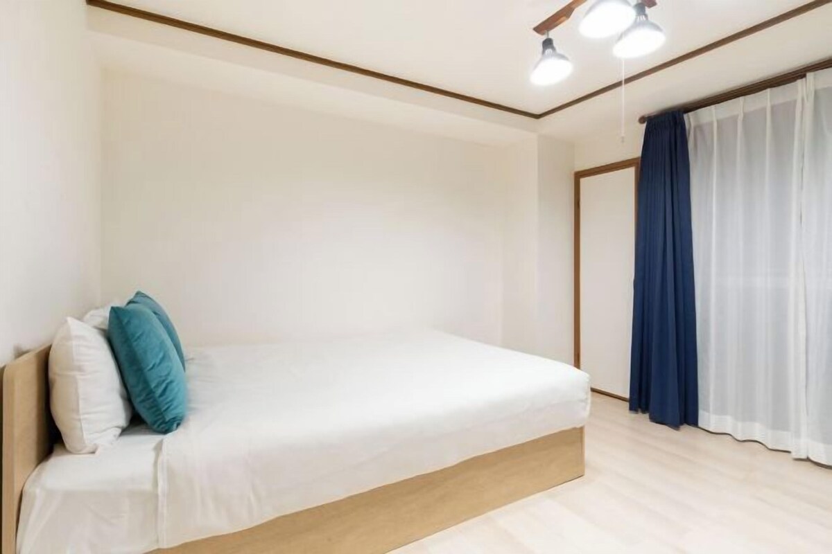 A bedroom with a single bed, a wooden headboard, a white mattress, and a blue curtain.