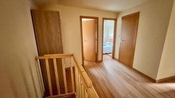 A hallway with wooden flooring, a wooden railing, and two doors leading to another room.