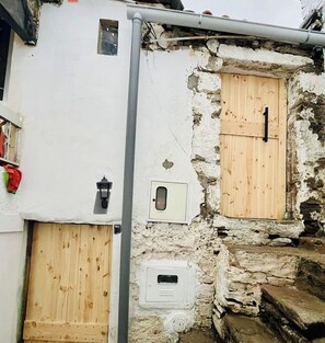 Ein rustikales Gebäude mit einer Holztür, einem kleinen Fenster mit Riegel und einer weißen Stromdosenleiste.
