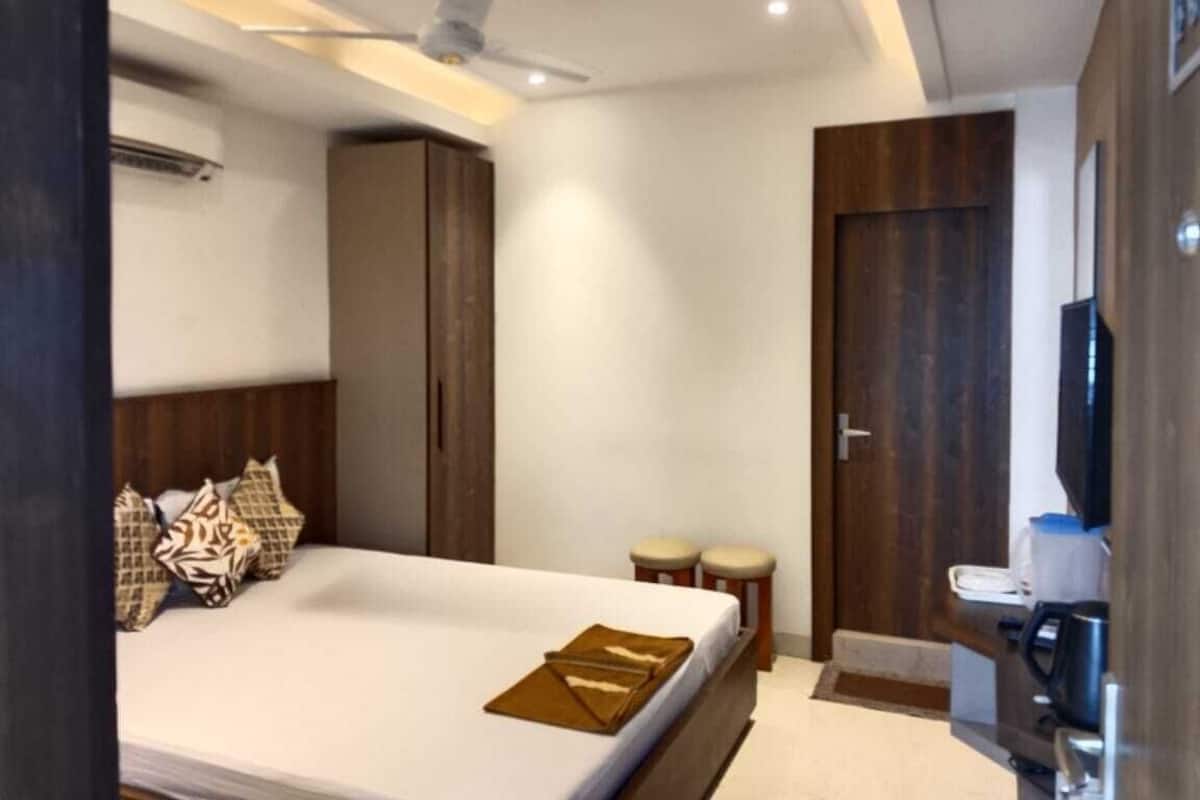 Quarto de hotel moderno com cama, ventoinha no teto, guarda-roupa, um espaço de estar pequeno e uma casa de banho.