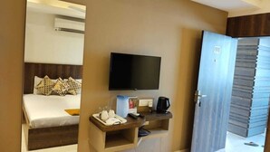 Habitación de hotel con una cama, televisor, cafetera y un escritorio pequeño con teléfono y vasos.
