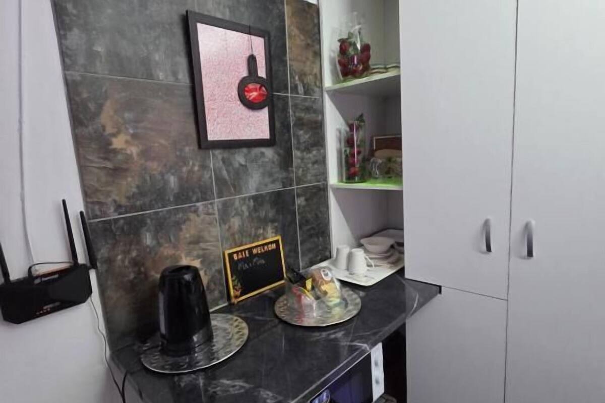 A compact kitchenette with a marble countertop, a coffee machine, a small refrigerator, and a shelf with decorative items.