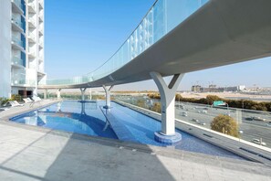Zwembad met een glazen brug, een wolkenkrabber en een snelweg op de achtergrond.