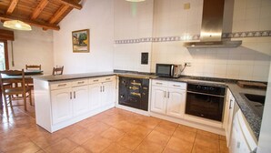 Une cuisine avec des meubles blancs, un four à micro-ondes, un four traditionnel et un plafond en bois.