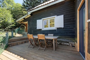 A wooden deck with a table and chairs, a window with shutters, and a door.