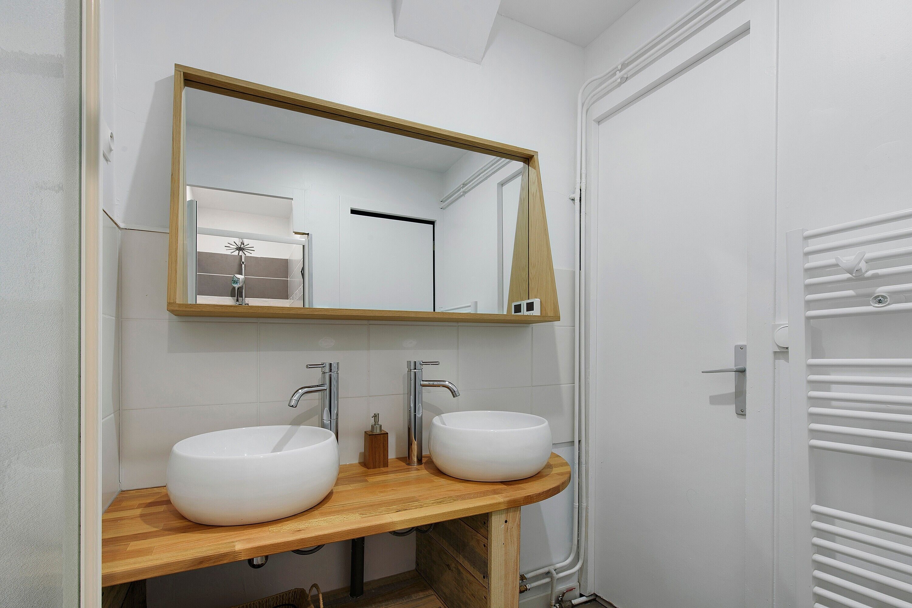 Een badkamer met twee witte wasbakken, een houten wastafelmeubel, een spiegel en een handdoekrek.