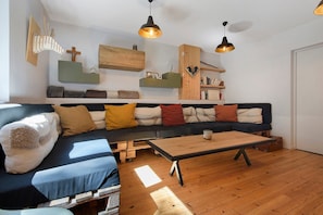 A modern living room with a sectional sofa, wooden flooring, and pendant lighting.
