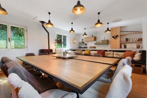 Ein modernes Interieur mit einem großen Holztisch, verschiedenen Sitzmöglichkeiten, Pendelleuchten und einem Bücherregal.