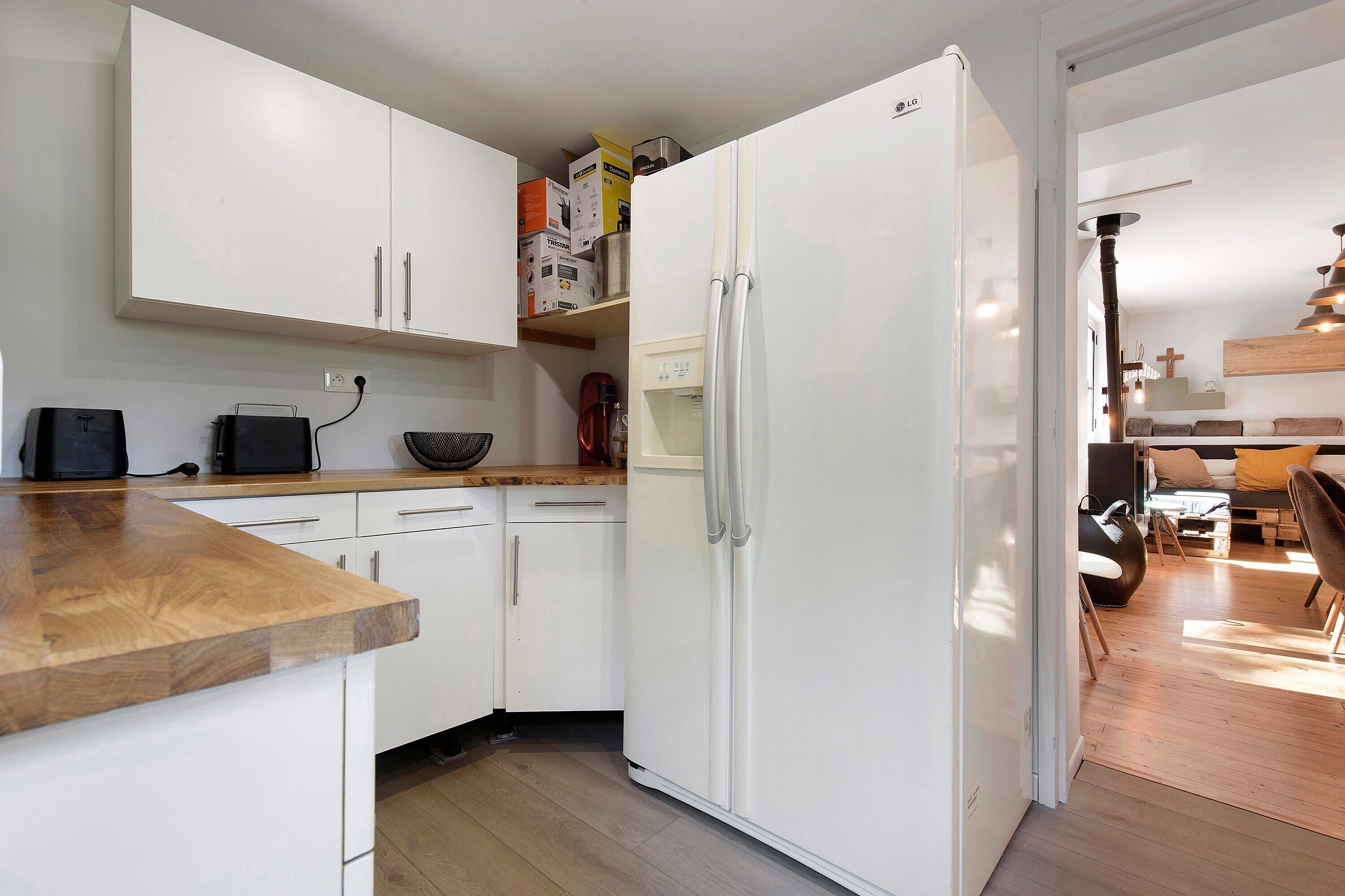 A modern kitchen with white cabinets, a wooden countertop, and a built-in refrigerator.