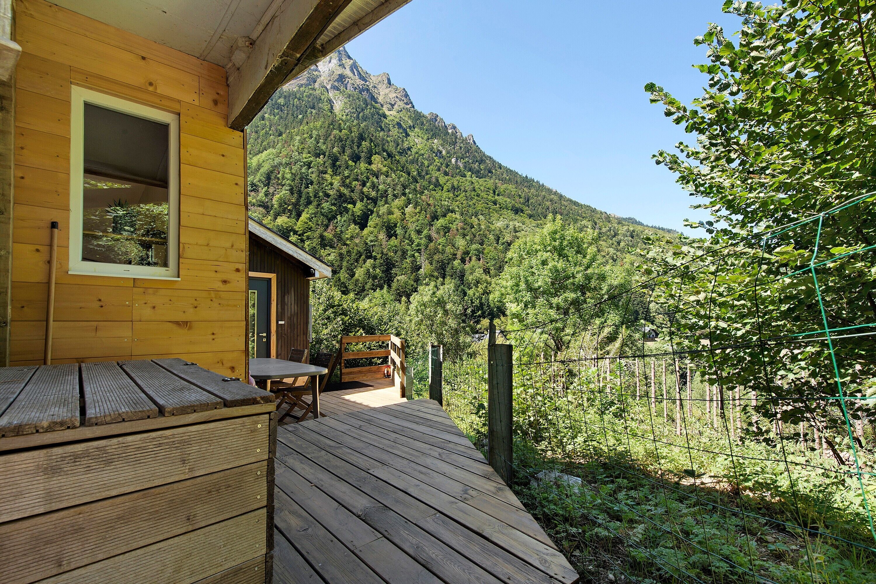 Eine Holzterrasse mit Tisch und Stühlen mit Blick auf einen bewaldeten Berg.
