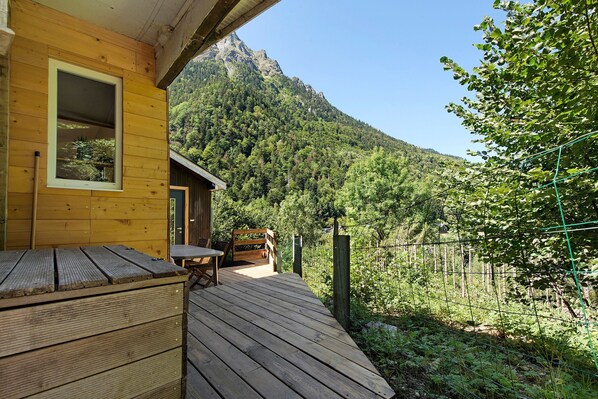A wooden deck with a table and chairs, overlooking a forested mountain.