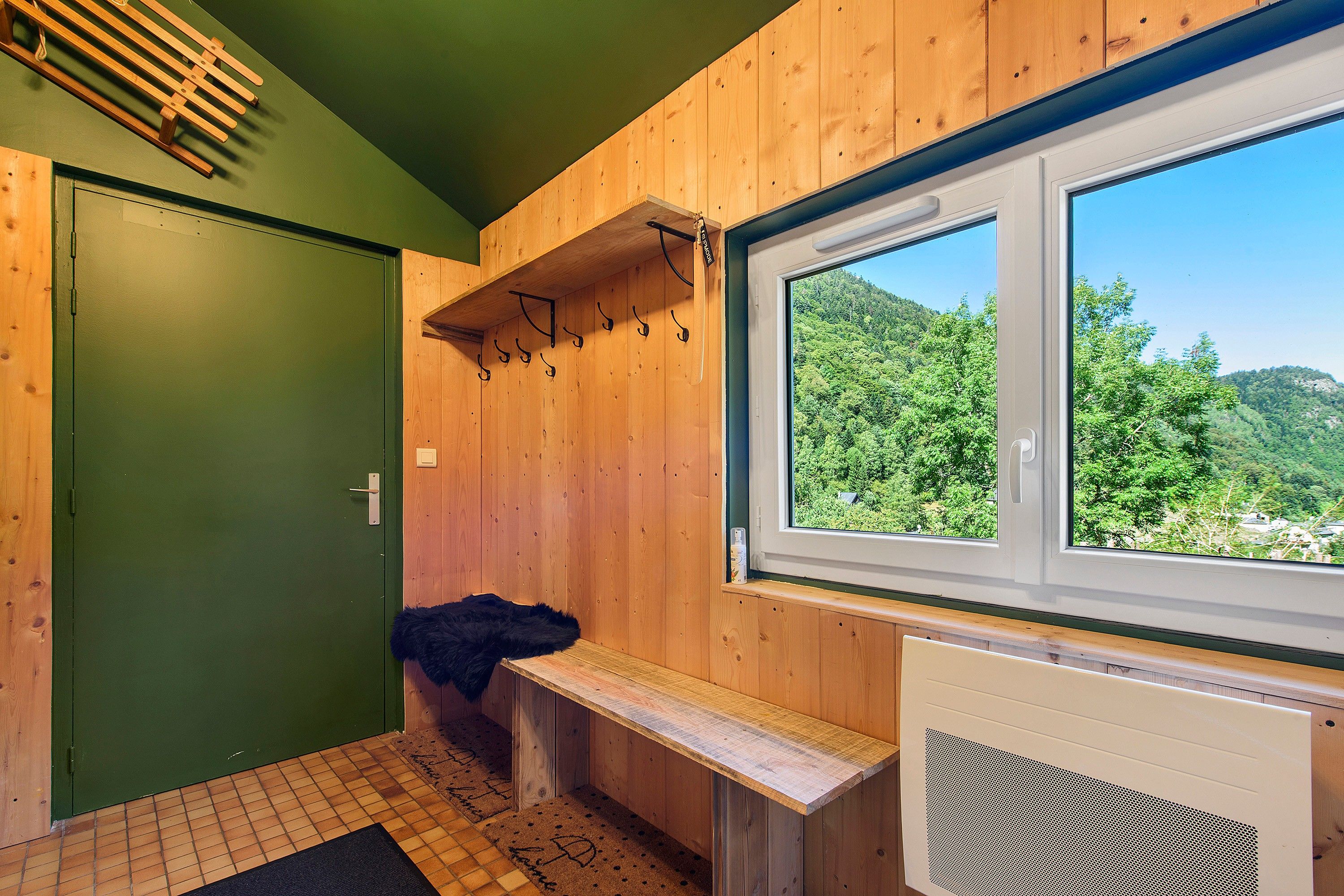 Ein Holzsaunaraum mit einer Bank, einem Fenster mit Blick auf einen Wald und einer grünen Tür.