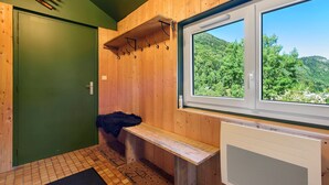 Un sauna en bois, avec un banc, une fenêtre donnant sur une forêt et une porte verte.