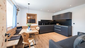 Een moderne keuken met donkere kastjes, een eethoek met houten meubels en een grijze bank.