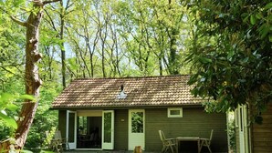 Une cabane rustique avec un toit en tuiles, une véranda avec des chaises et une petite table.