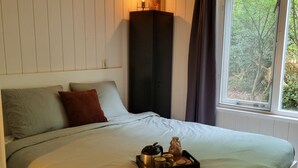 Un lit avec un plateau de petit-déjeuner, une armoire, une fenêtre donnant sur des arbres et une lampe fixée au mur.