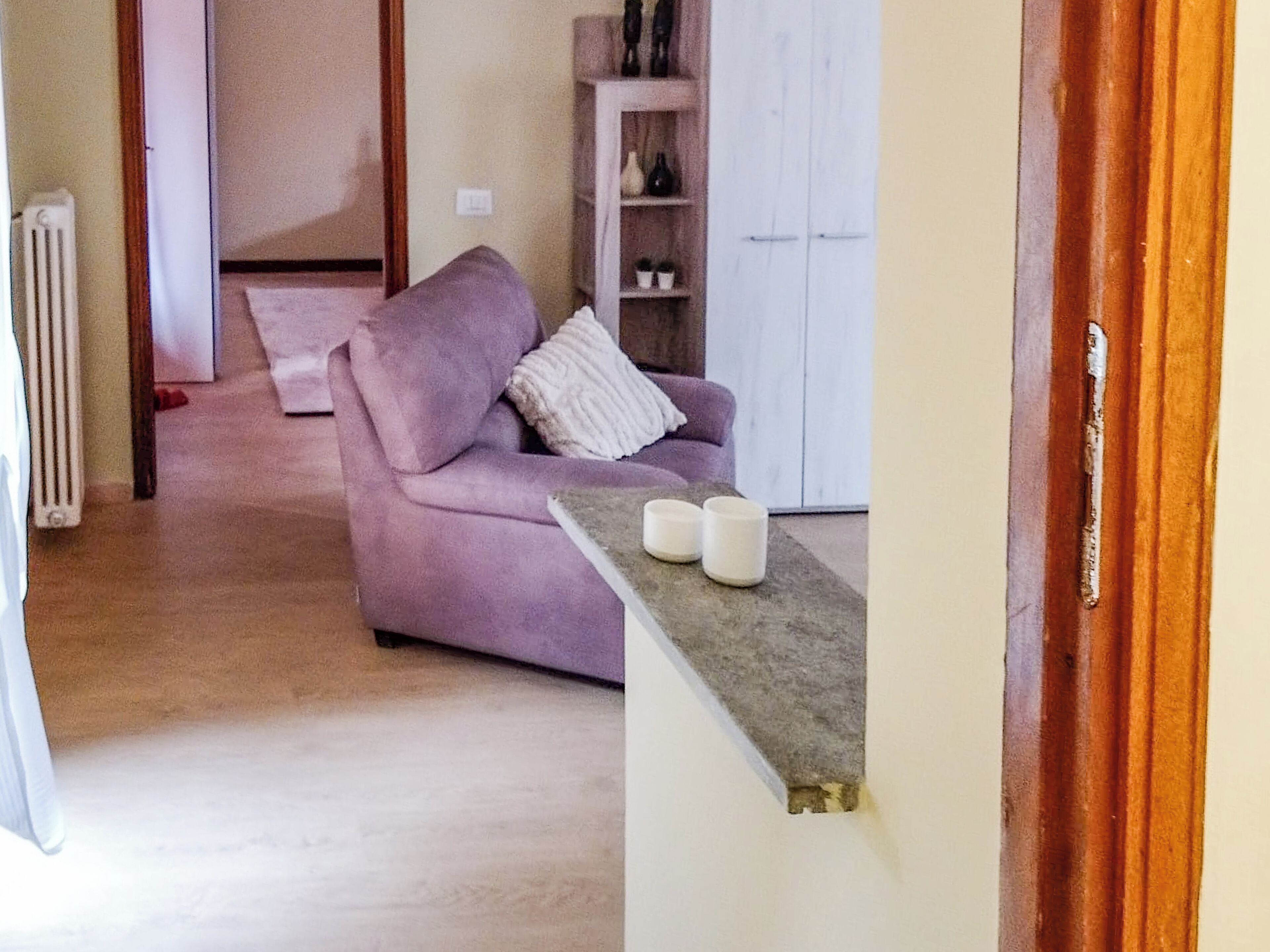 Un salon avec un canapé violet, un meuble blanc et une petite table sur laquelle sont posées deux bougies blanches.
