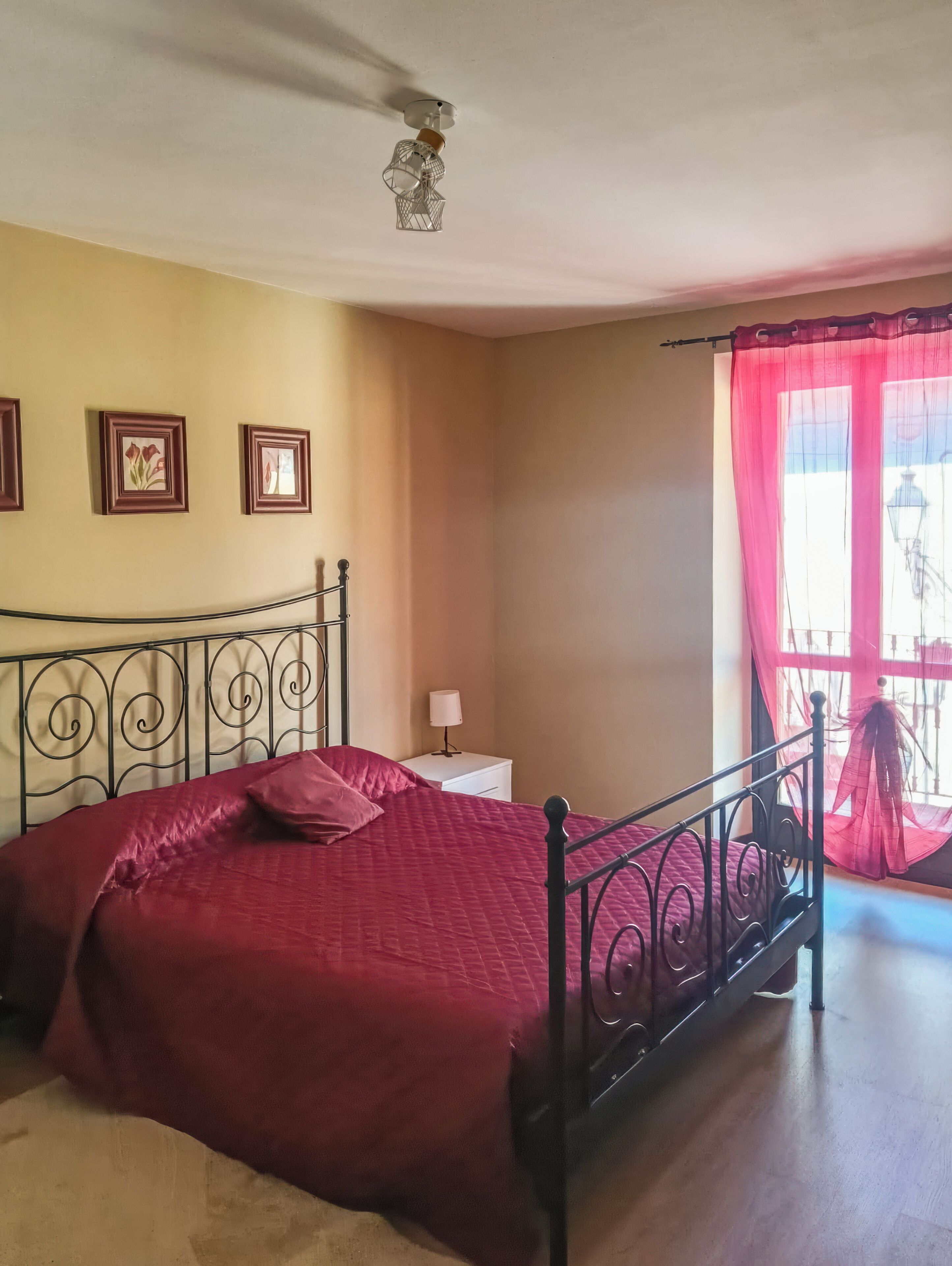 Un dormitorio con una cama, una mesita de noche, una lámpara y una ventana con cortinas.