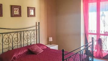 Un dormitorio con una cama, una mesita de noche, una lámpara y una ventana con cortinas.