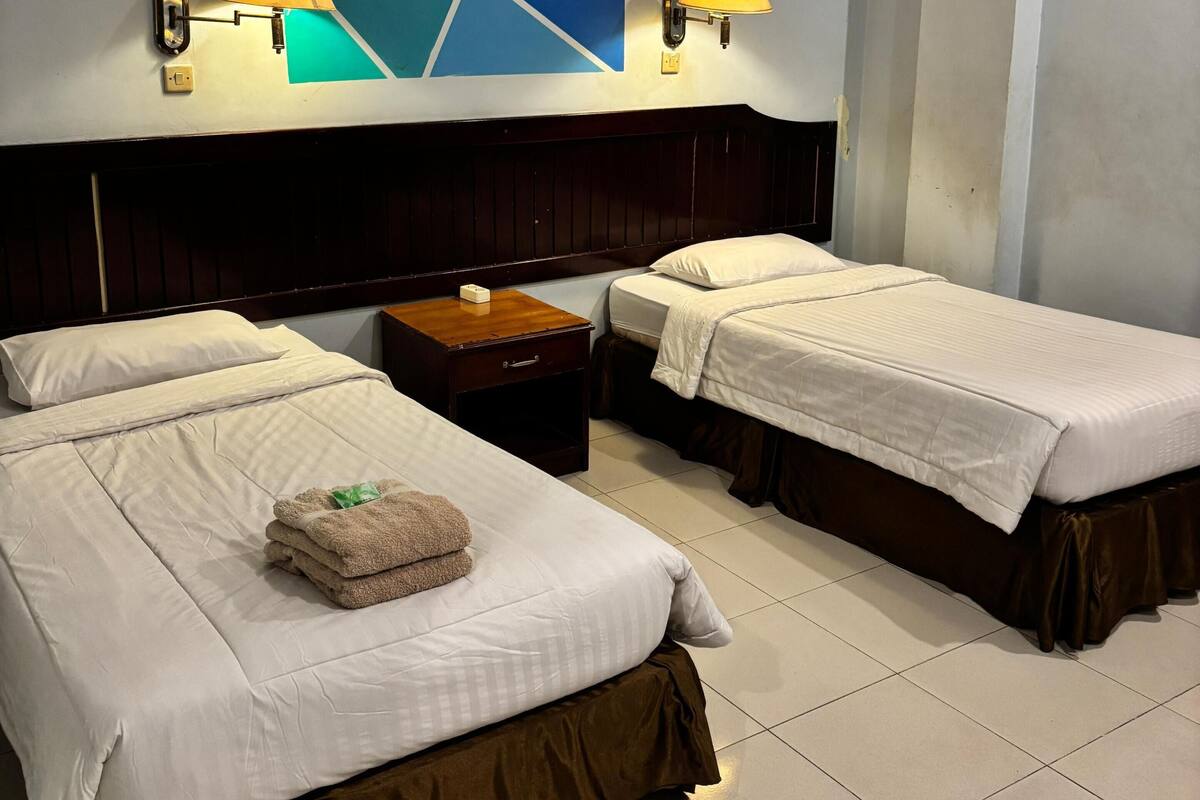 Ein Hotelzimmer mit zwei Betten, einem Wandbild, zwei Wandleuchten, einem Nachttisch aus Holz und einem gefliesten Boden.