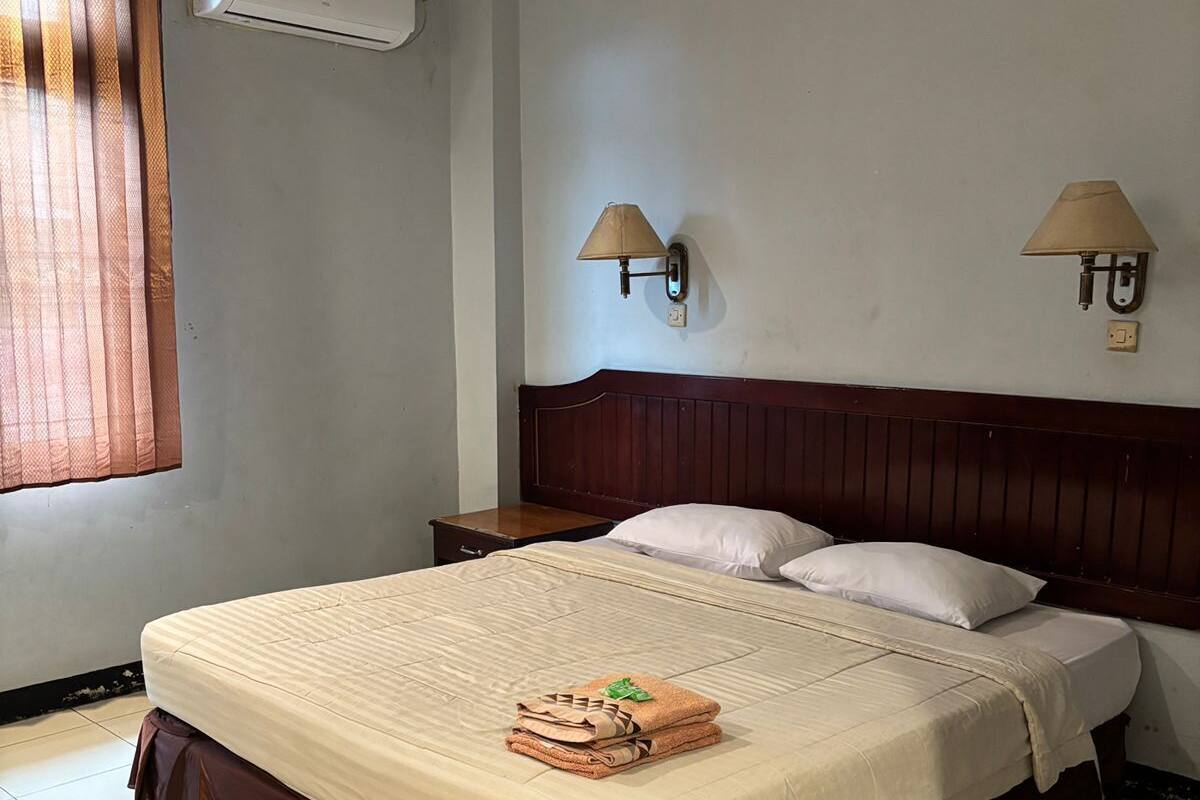 Ein Hotelzimmer mit einem Bett, zwei Wandleuchten, einer Klimaanlage und einem Fenster mit Vorhängen.