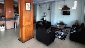 Un salón amplio con un pilar de madera, sofás negros, una mesa de centro y un televisor montado en la pared.