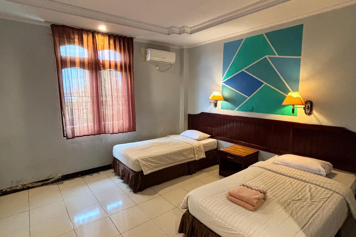 Ein Hotelzimmer mit zwei Betten, einem fensterbelaubten Fenster, einer Klimaanlage und einer geometrischen Wanddekoration.