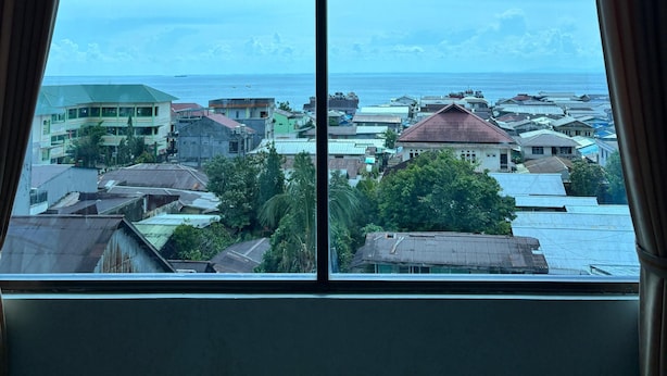 Una ventana con vista a un pueblo costero, edificios y el mar.