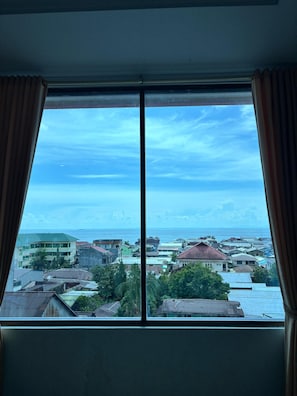 A window with a view of a coastal town, buildings, and the sea. - Hotel Grand Taufiq Tarakan (Tarakan)