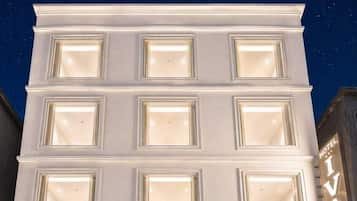Un hotel con fachada moderna, varias ventanas iluminadas y una recepción con espacio interior a la vista.