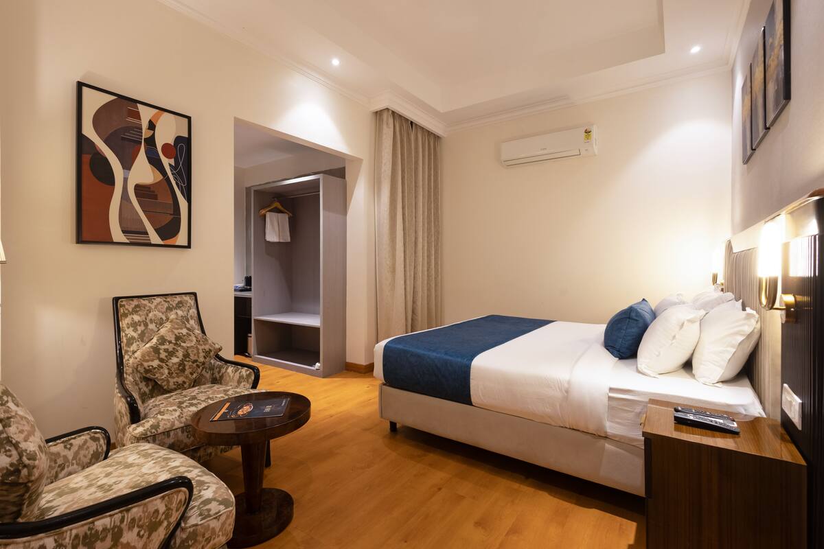 Habitación de hotel con cama, una silla, una mesita y un cuadro en la pared.