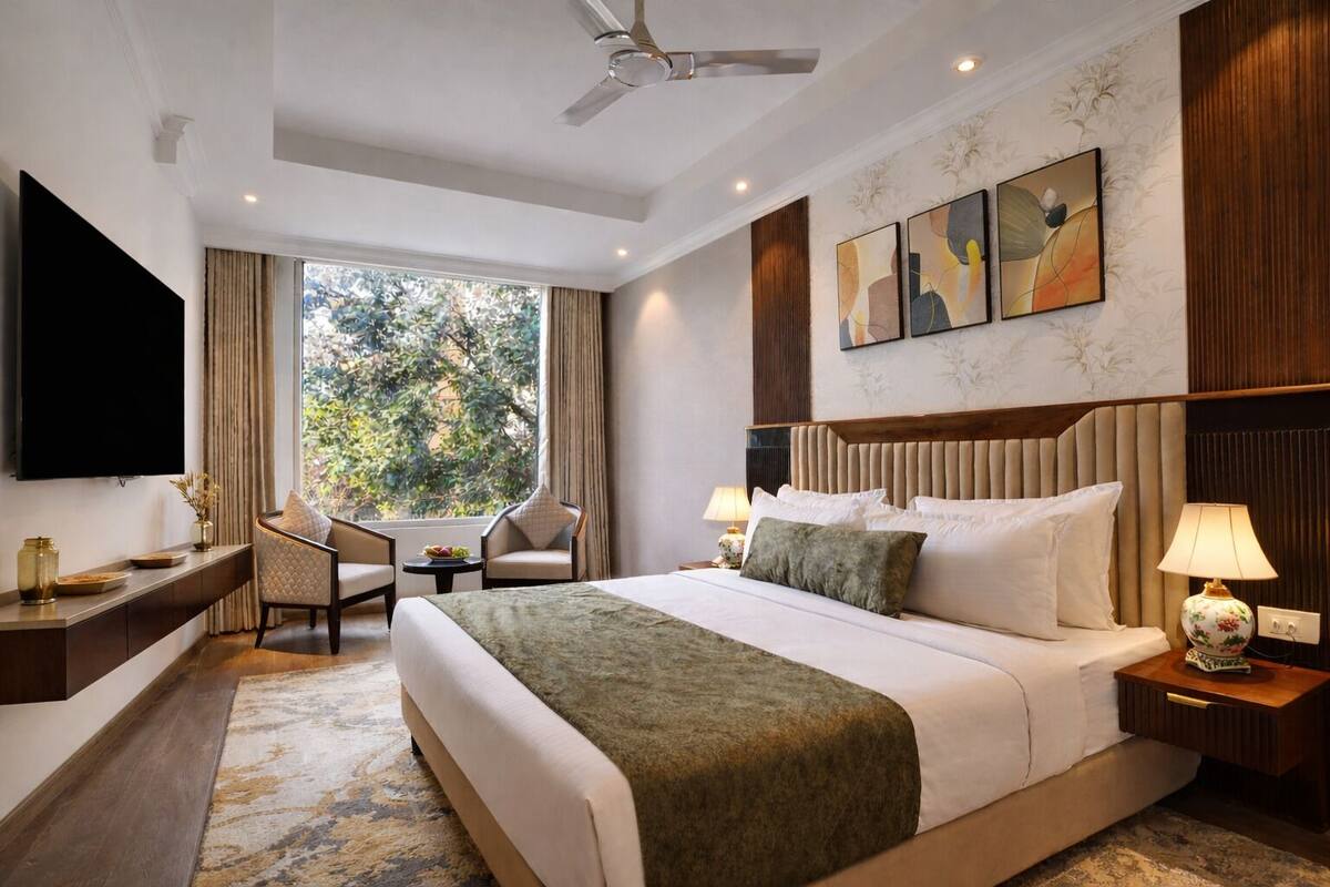 Habitación de hotel con cama, mesitas de noche, televisor, escritorio, silla y ventana con vistas a árboles.