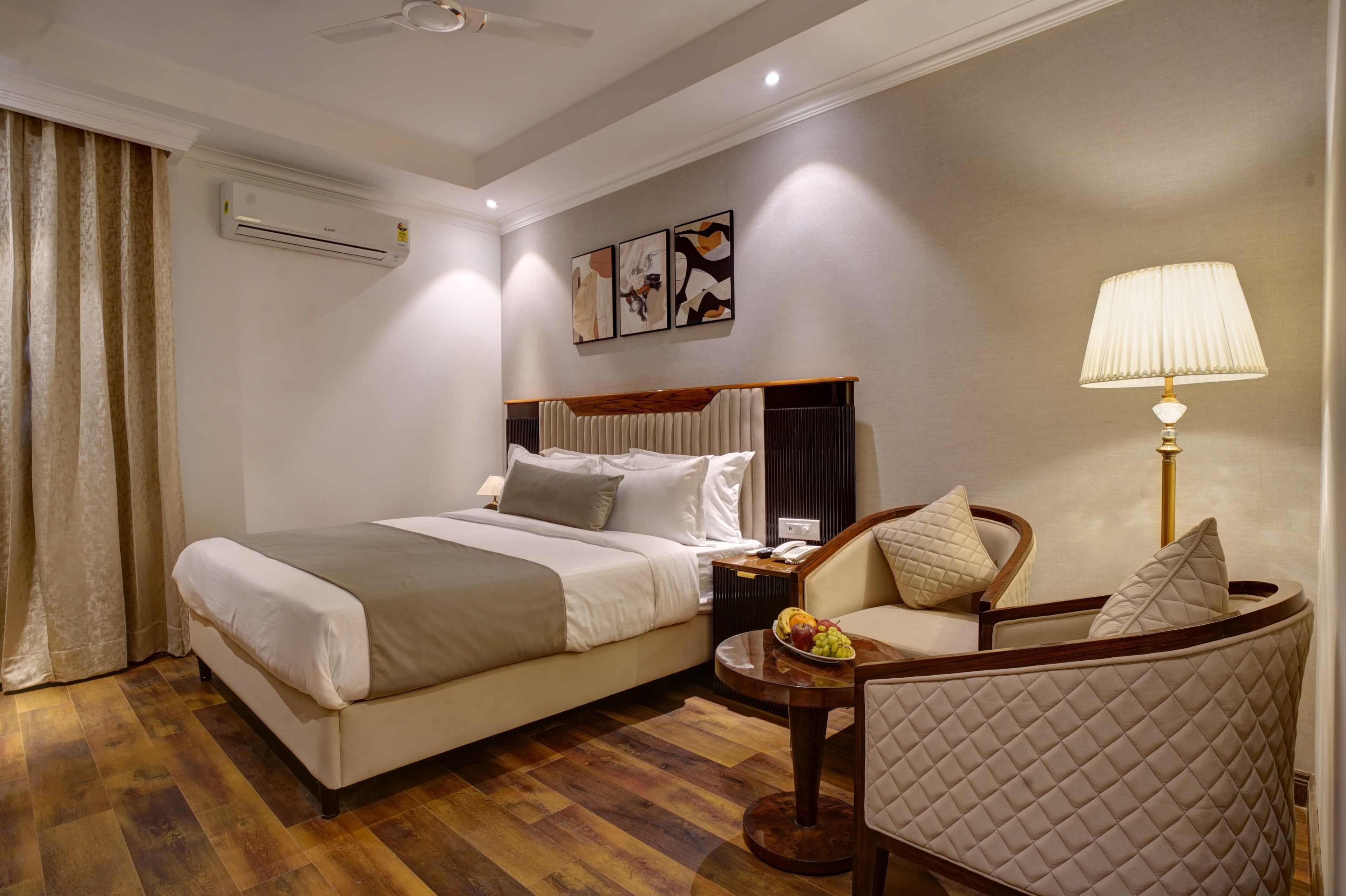 Ein Hotelzimmer mit einem Bett, einem Sessel, einem kleinen Tisch mit Früchten, einer Klimaanlage und Bildern an der Wand.