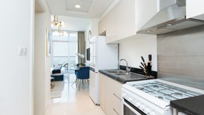 Een moderne keuken met een gasfornuis, een spoelbak van roestvrij staal en een eethoek met een blauwe stoel en een kleine tafel.