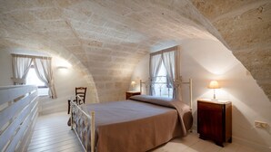 Una camera da letto con soffitto spiovente, un letto, un comodino, una sedia e una finestra con tende.