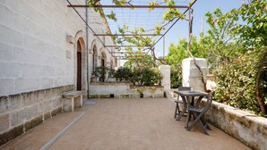 An outdoor patio with a table and chairs, a pergola with vines, and a stone wall. - Lamapecora - Salone Apartment with Balcony, Wi-Fi and Air Conditioning (Fasano)