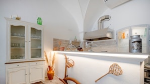 A kitchen with a white cabinet, a wooden utensil leaning against the wall, and a modern stove. - Lamapecora - Salone Apartment with Balcony, Wi-Fi and Air Conditioning (Fasano)