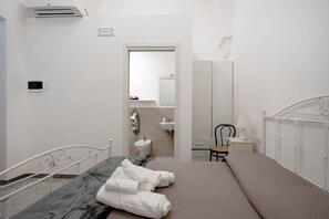 A bedroom with a bed, a bedside table, a chair, a wardrobe, a mirror, and a bathroom with a sink and toilet. - Room 'Lamapecora - Pecora 2' with Balcony, Wi-Fi and Air Conditioning (Fasano)