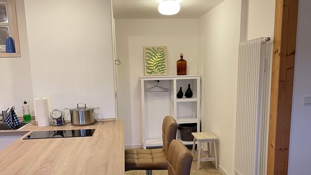 Una cocina moderna con encimera de madera, dos sillas de cuero marrón, un estante blanco con adornos y un radiador blanco.