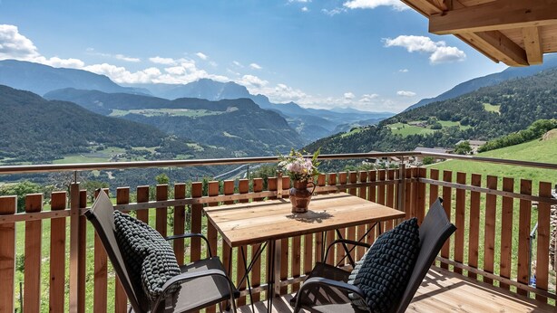 Een houten terras met een tafel en stoelen, met uitzicht op een bergachtig landschap.