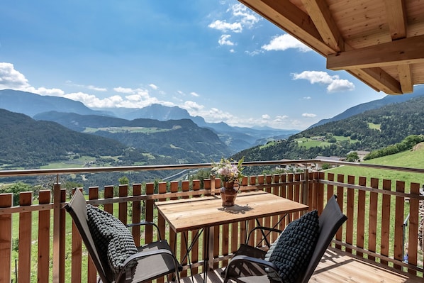 Eine Holzterrasse mit Tisch und Stühlen mit Blick auf eine gebirgige Landschaft.