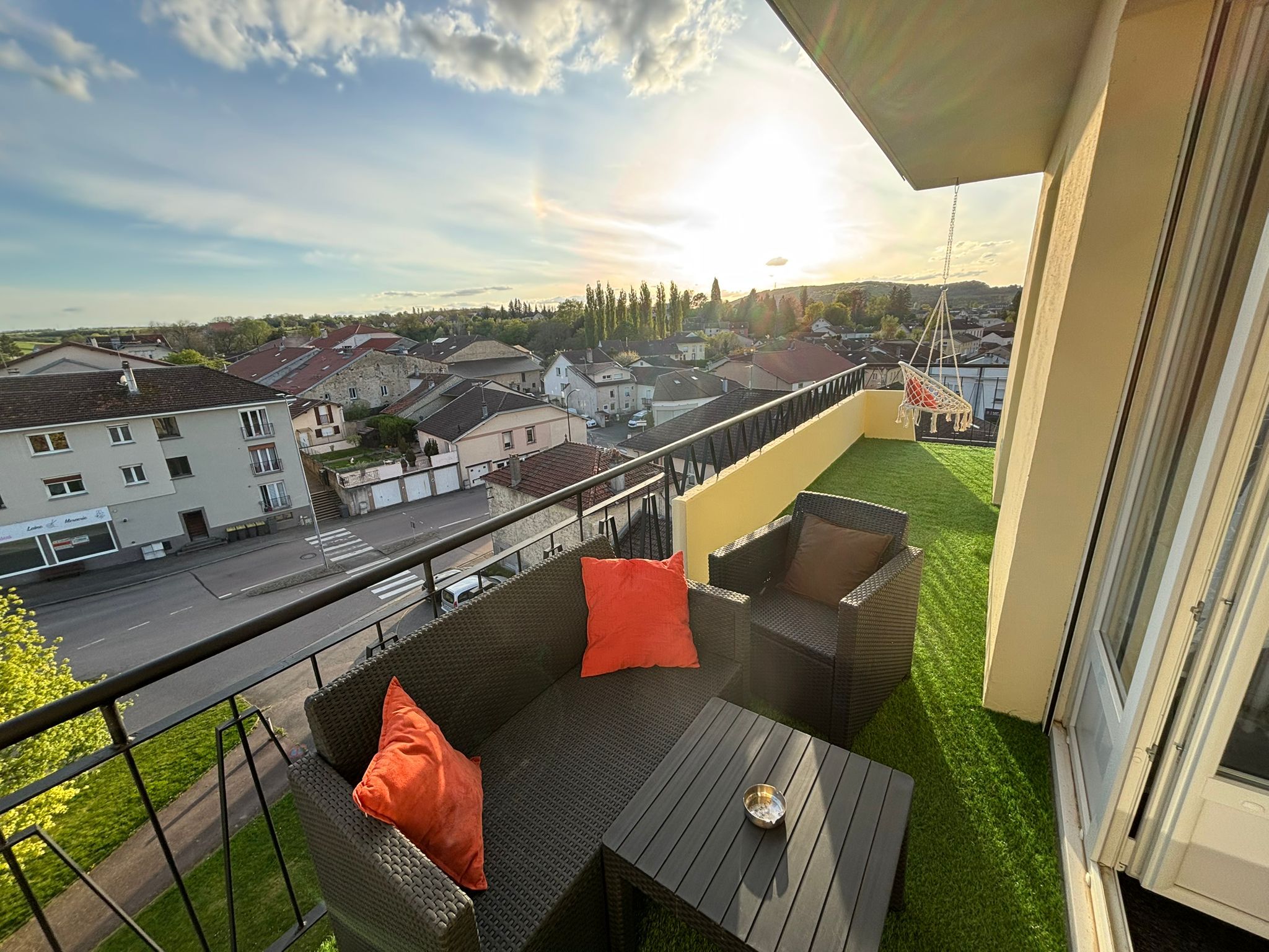Varanda com móveis de exterior, vista para a rua e um pôr do sol.